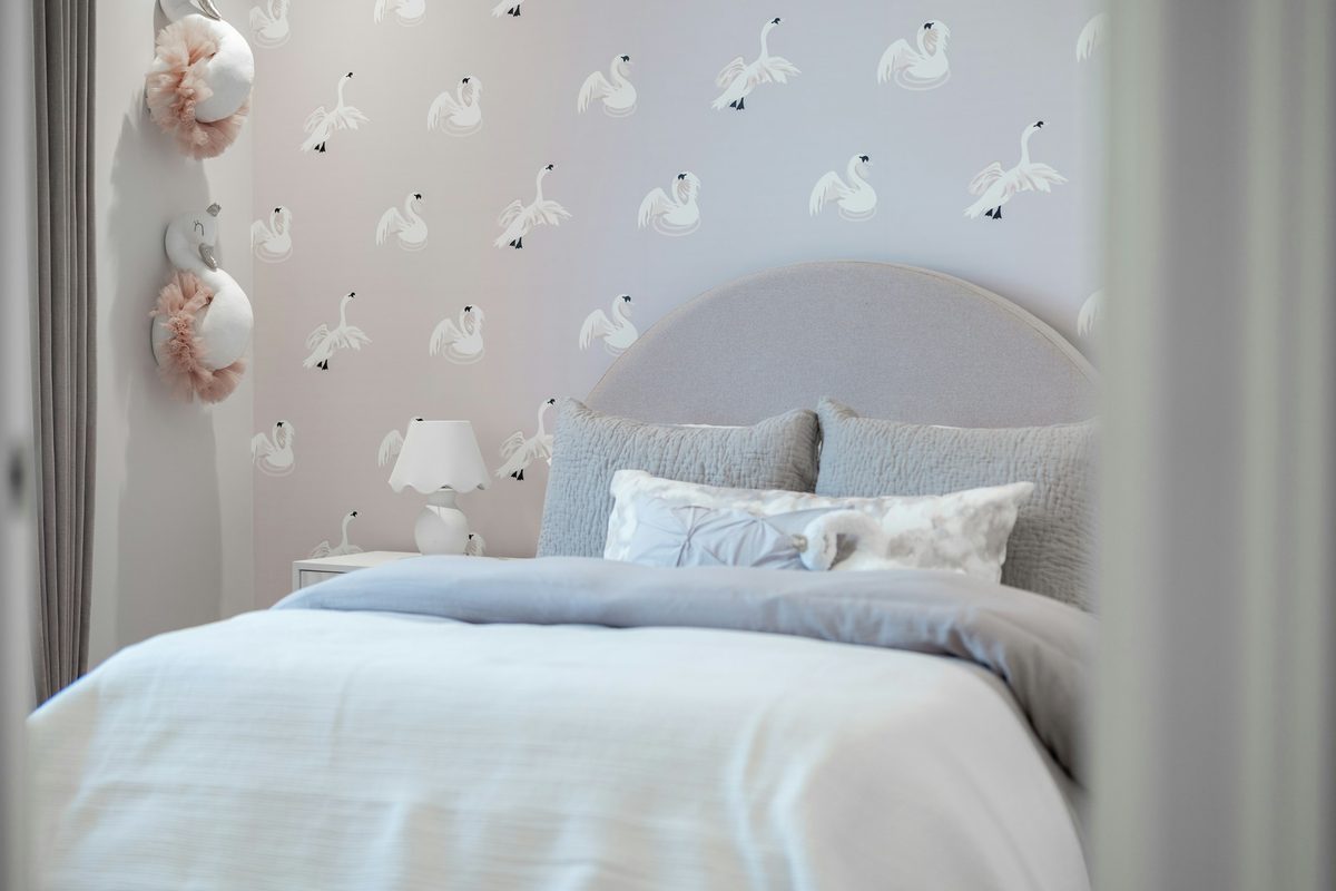 Bedroom with a delicate swan-pattern wallpaper behind an upholstered headboard.
