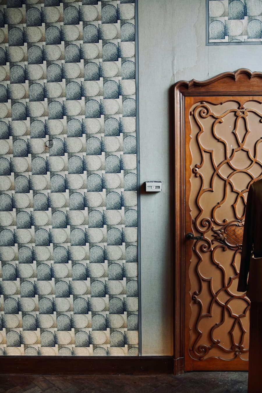 Close-up of a geometric patterned wallpaper meeting a carved wooden door.