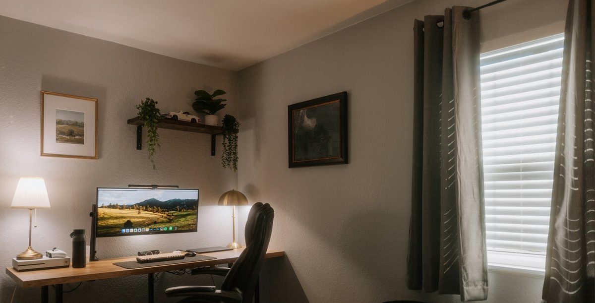 Home office corner with a wood desk, floating shelf, and framed artwork.