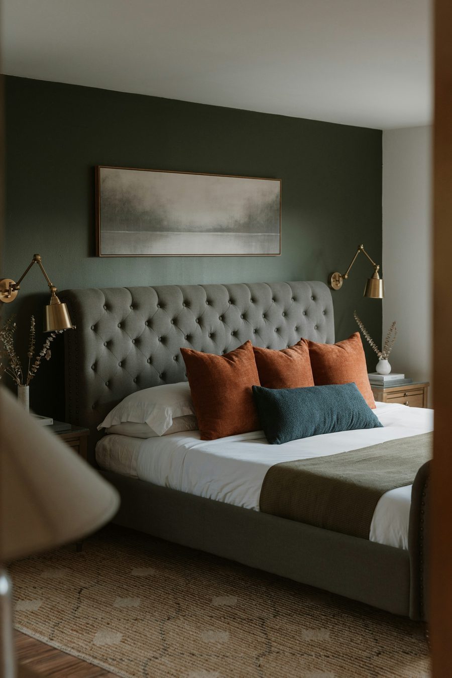 Bedroom with a deep green accent wall, tufted headboard, and brass sconces.